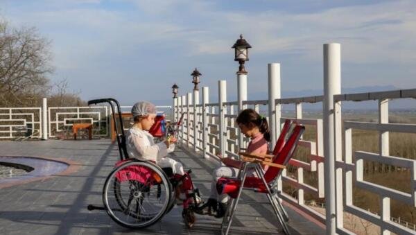 Imatge il·lustrativa d'inclusió i accessibilitat: una noia en cadira de rodes conversant amb una amiga en un parc
